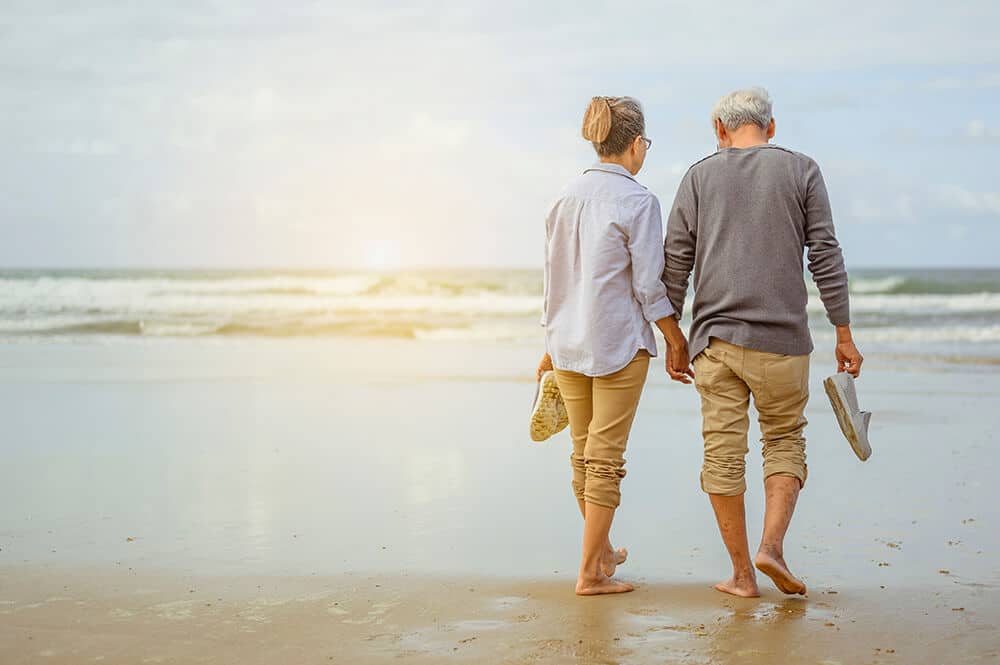 older couple walking on a beach contemplating retirement
