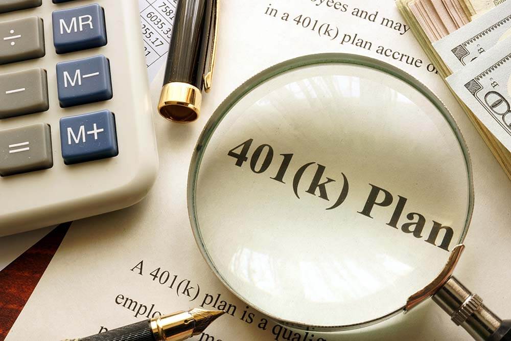 paper with the printed words 401(k) plan with a magnifying glass on top of it